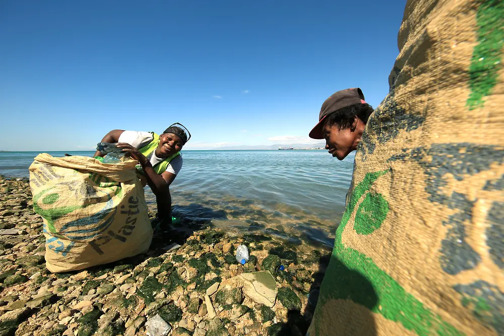 Proyecto “Plastic Bank”: dos personas recogiendo plástico en una playa.
