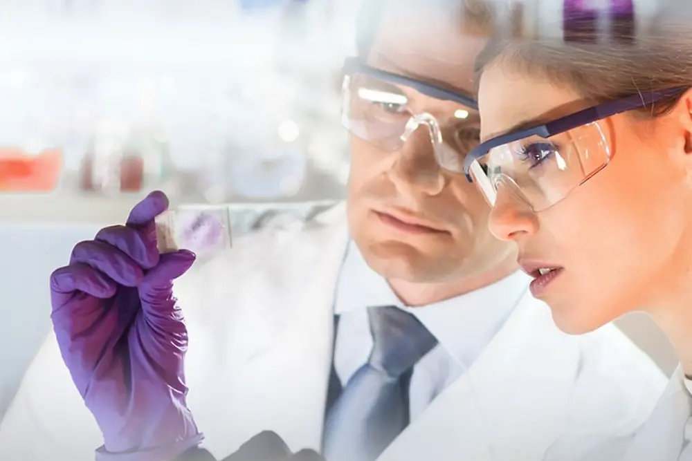 Rostros de una mujer y un hombre observando una muestra en un laboratorio.