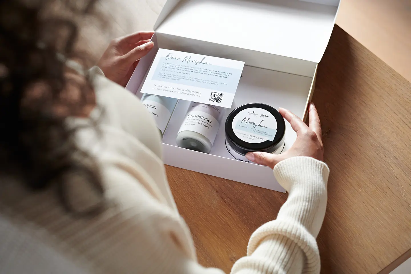 A woman has the opened SalonLab&Me product package in front of her, which contains personalized products.