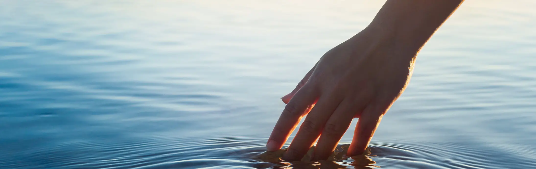 Una mano acaricia una tranquila superficie de agua frente al horizonte.