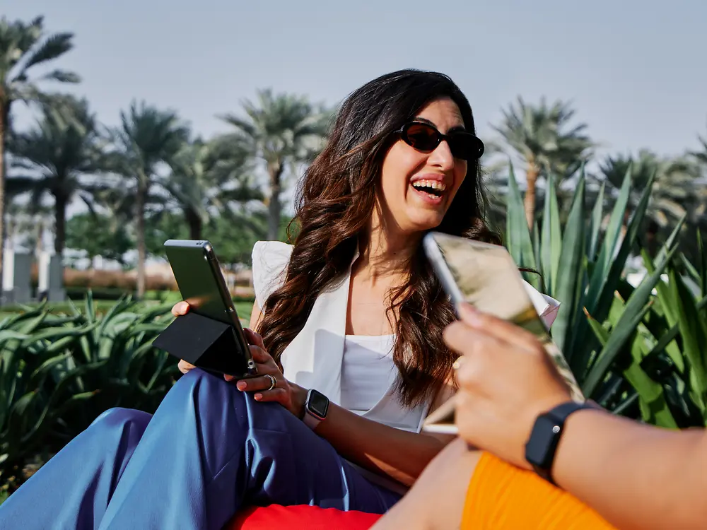 Una mujer trabajando con una computadora portátil al aire libre en un parque soleado, lo que refleja las opciones de trabajo flexibles y la cultura laboral moderna de Henkel.