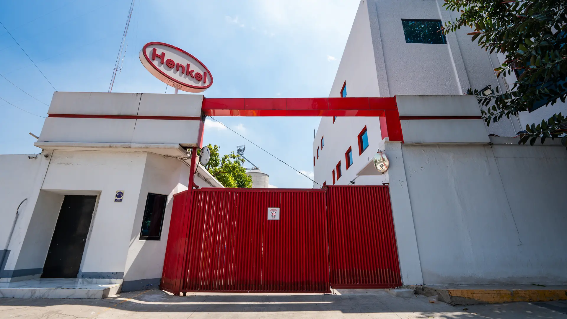 Fachada del Centro Especializado Vallejo de Henkel con portón metálico rojo y estructura blanca. El logotipo de Henkel se encuentra sobre la entrada principal.
