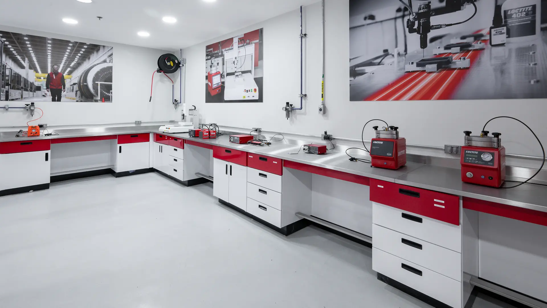 Interior del Centro de Entrenamiento y Aplicación en Reparación Vehicular con paredes blancas y rojas, mesas de trabajo metálicas, herramientas y carteles promocionales. Se observa un automóvil negro con el cofre abierto en una zona de servicio.