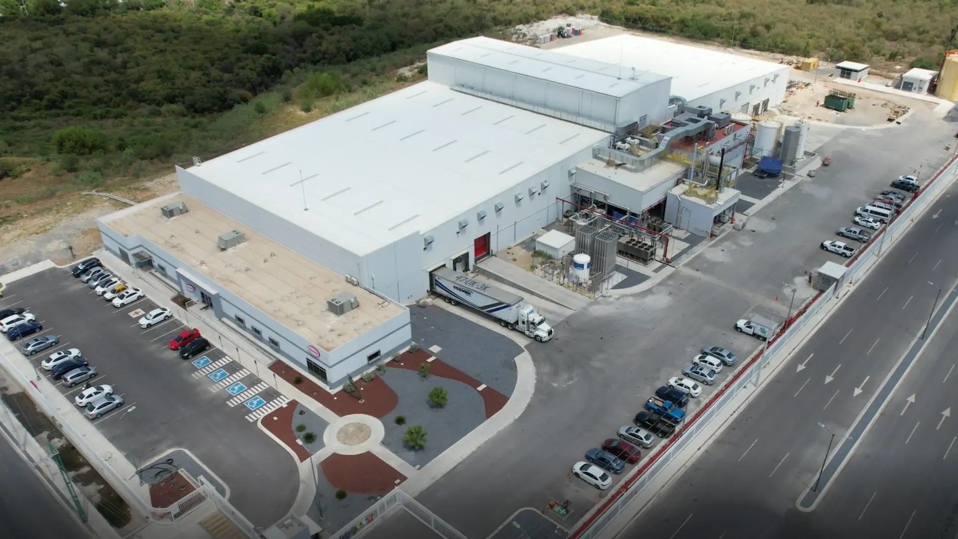 Vista aérea de la planta Guadalupe con techos blancos y varias áreas anexas. Se observan estacionamientos con vehículos, zonas de carga con un tráiler en la rampa, estructuras metálicas y tanques en la parte trasera.