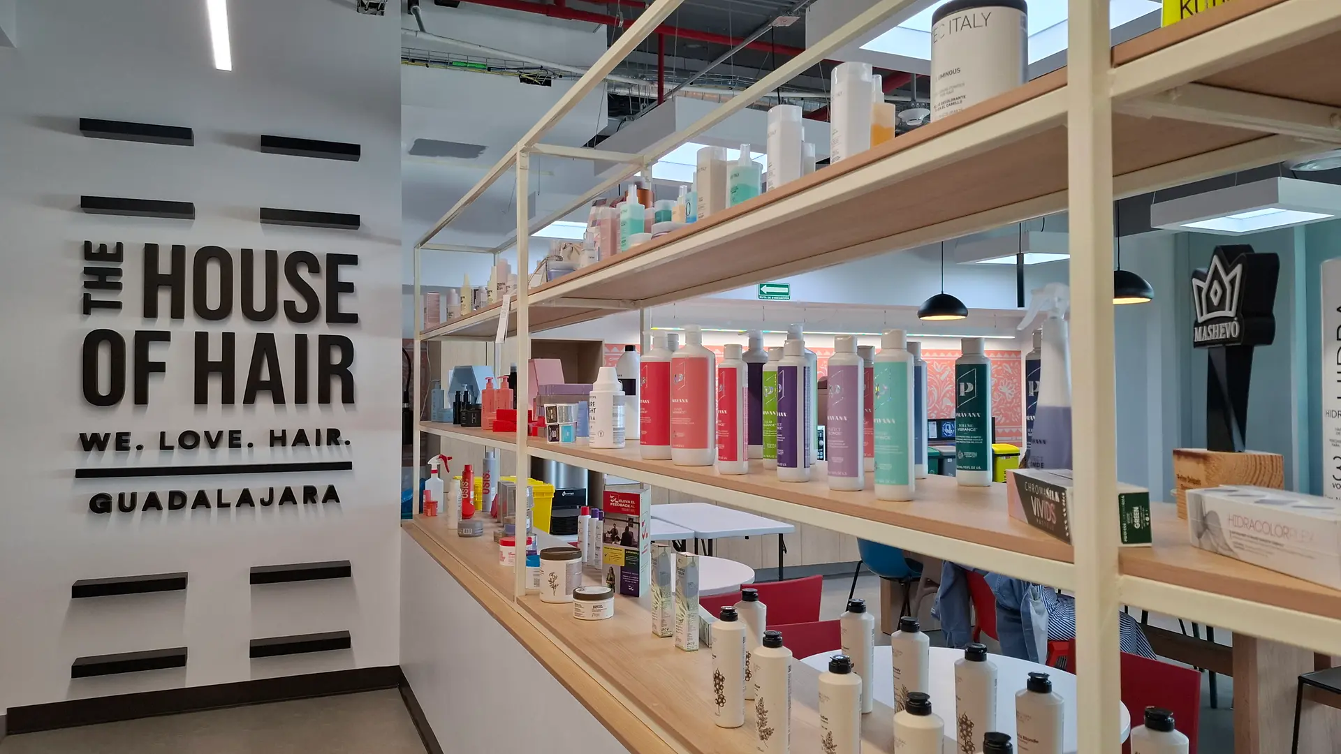 Vestíbulo moderno con una llamativa pared de exhibición que presenta grandes paneles con gráficos coloridos inspirados en el cabello y el texto: “THE HOUSE OF HAIR – WE. LOVE. HAIR. – GUADALAJARA”.