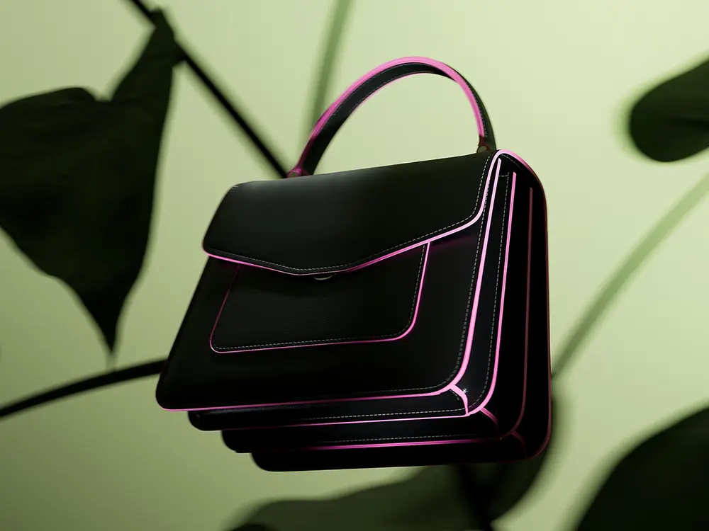 Bolso negro de diseño estructurado con bordes rosa brillante, mostrado sobre un fondo verde con hojas desenfocadas.