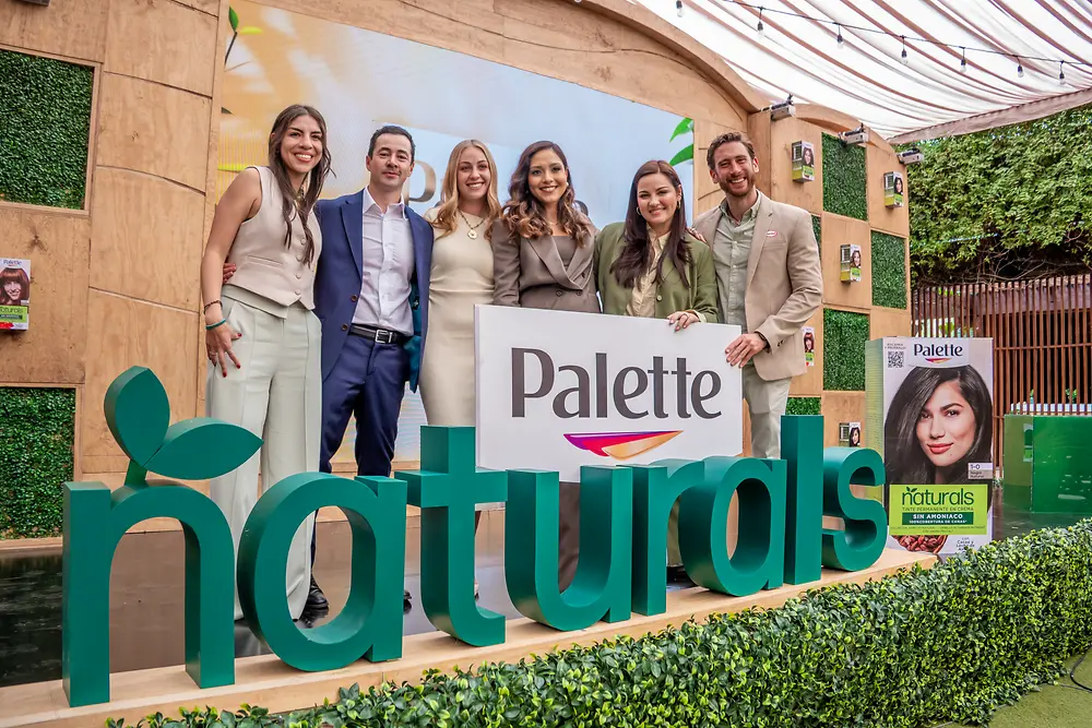 Grupo de personas en un escenario con elementos verdes y madera con un letrero del logo de “Palette”. En primer plano destaca una instalación con la palabra “naturals” en letras verdes.