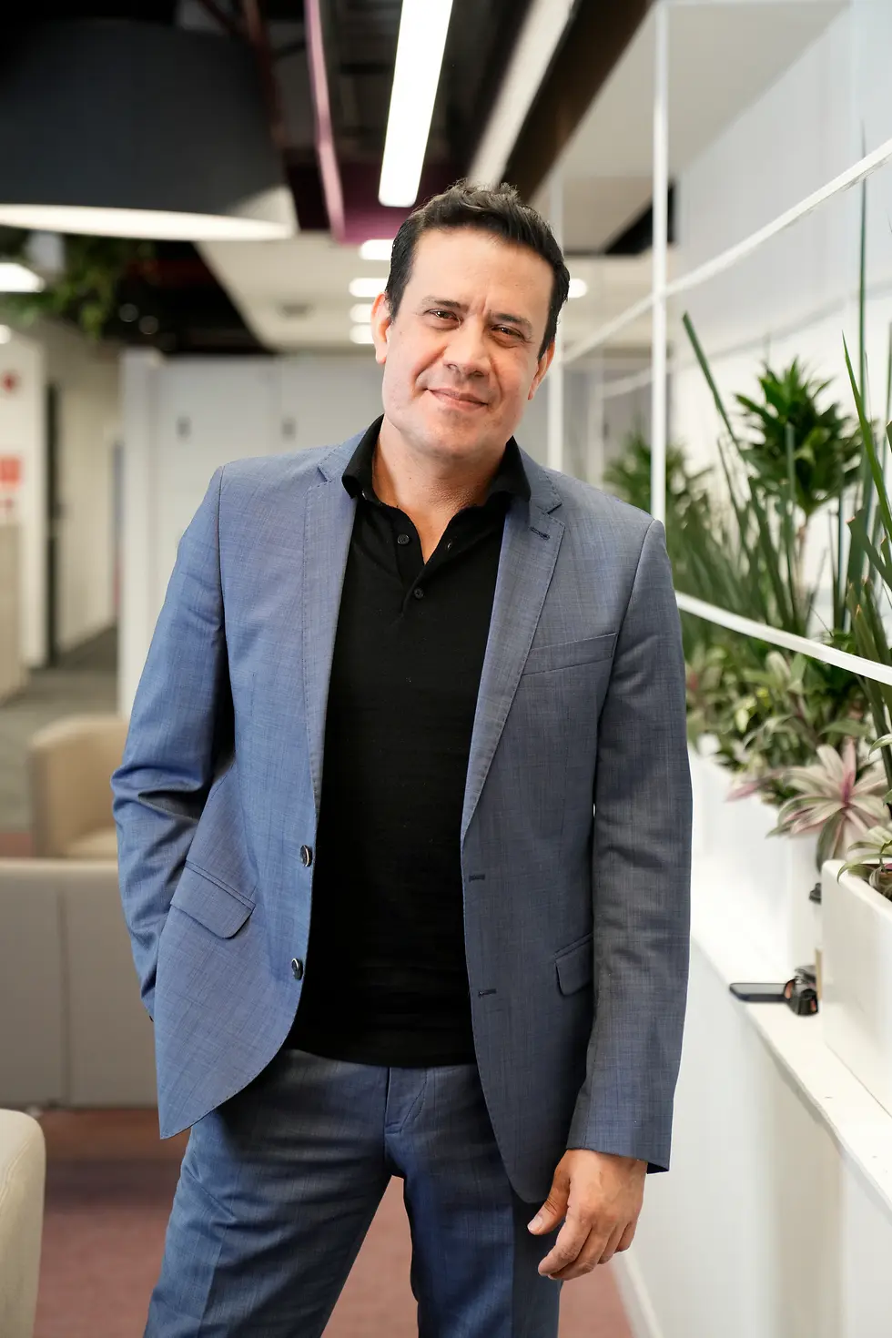 Retrato de persona vestida con traje azul y camisa oscura, en un espacio de oficina.